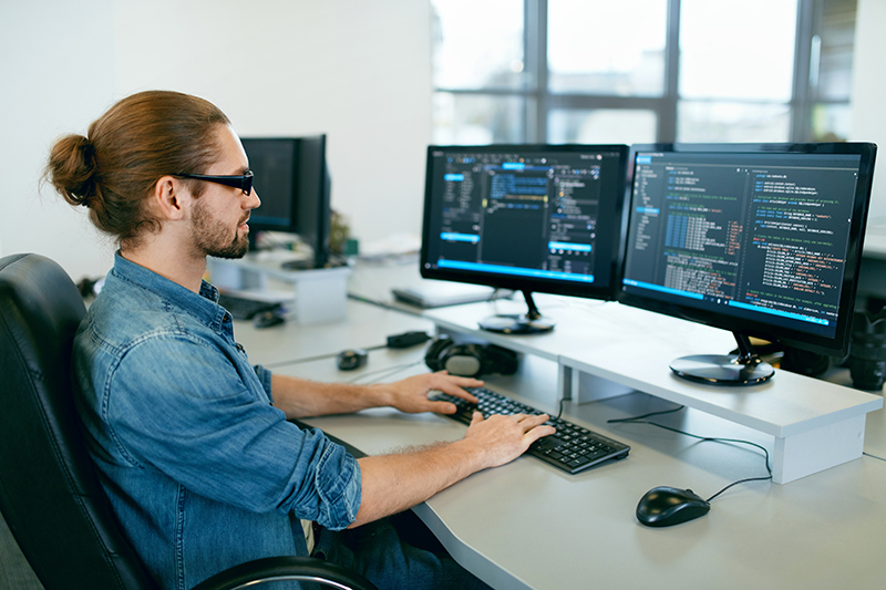 Programación. El hombre que trabaja en la computadora en la oficina de TI, sentado en el escritorio de escritura de códigos. Programador escribiendo código de datos, trabajando en un proyecto en una empresa de desarrollo de software. Imagen de alta calidad.