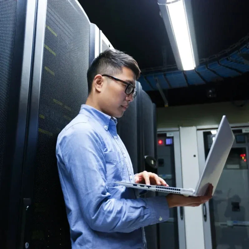 Technicus die storingen verhelpt op een laptop naast serverkasten, en ondersteuningsdiensten verleent voor AS/400 en iSeries